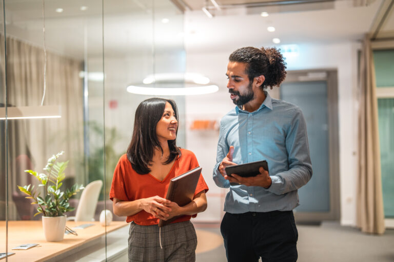 Attractive multiracial colleagues demonstrate their expertise and success in the corporate office, engaging in a productive meeting while utilizing wireless technology and a digital tablet. Their smart casual attire and professional demeanor showcase their commitment to success.