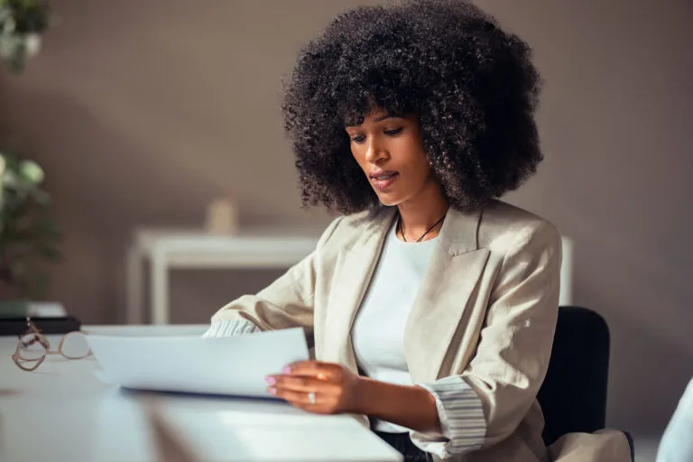 Professional businesswoman concentrating on reviewing documents at her office desk. She exudes confidence and determination in a modern work environment.